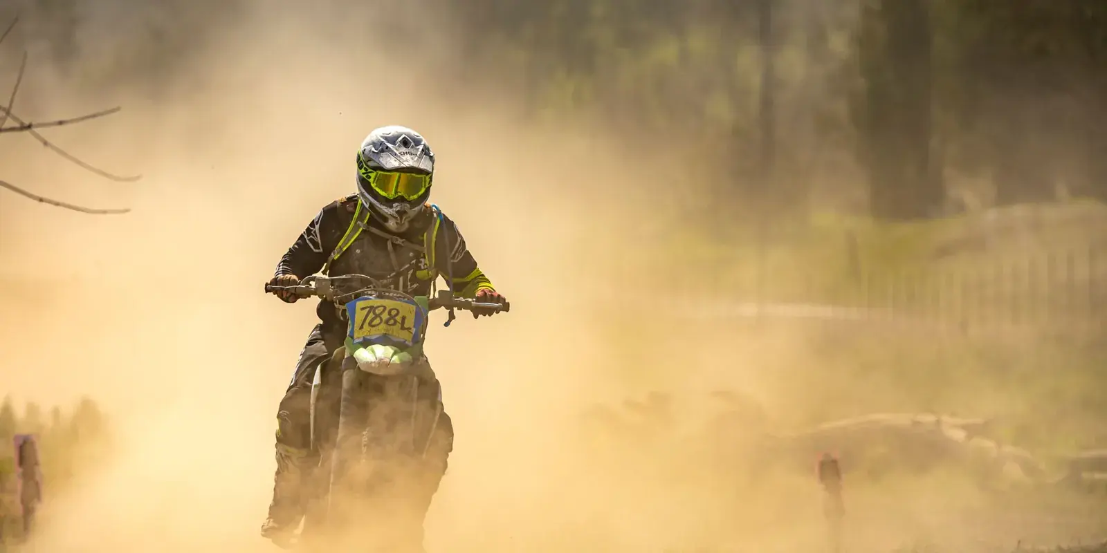 Un motociclista da enduro avanza in una nuvola di polvere dorata