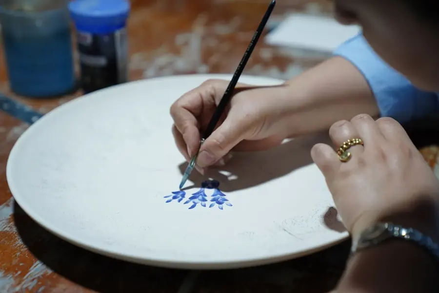 Mani che dipingono a pennello un motivo blu su un piatto di ceramica