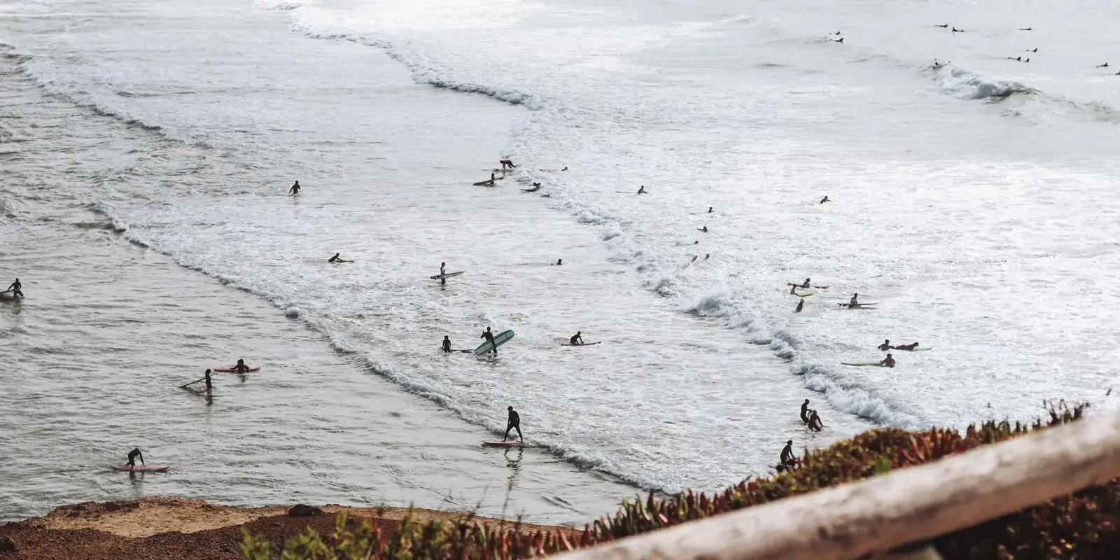 Surfisti tra le onde basse di una spiaggia atlantica visti dall'alto della falesia