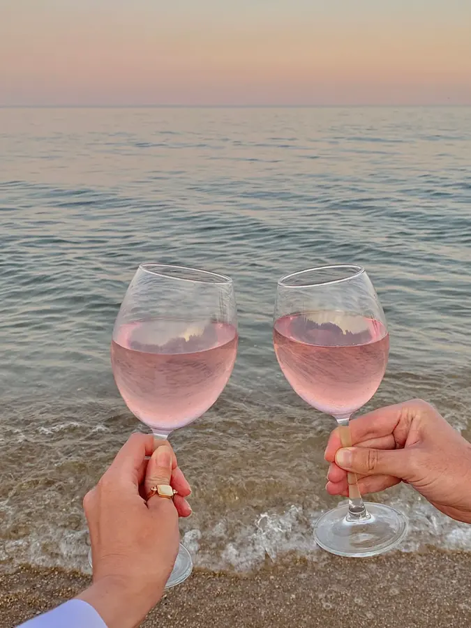 Due calici di vino rosato alzati in un brindisi sul bagnasciuga al tramonto