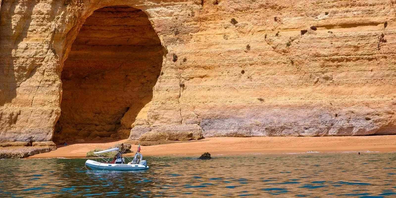 Una barca lungo le falesie dorate dell'Algarve, davanti a una grotta