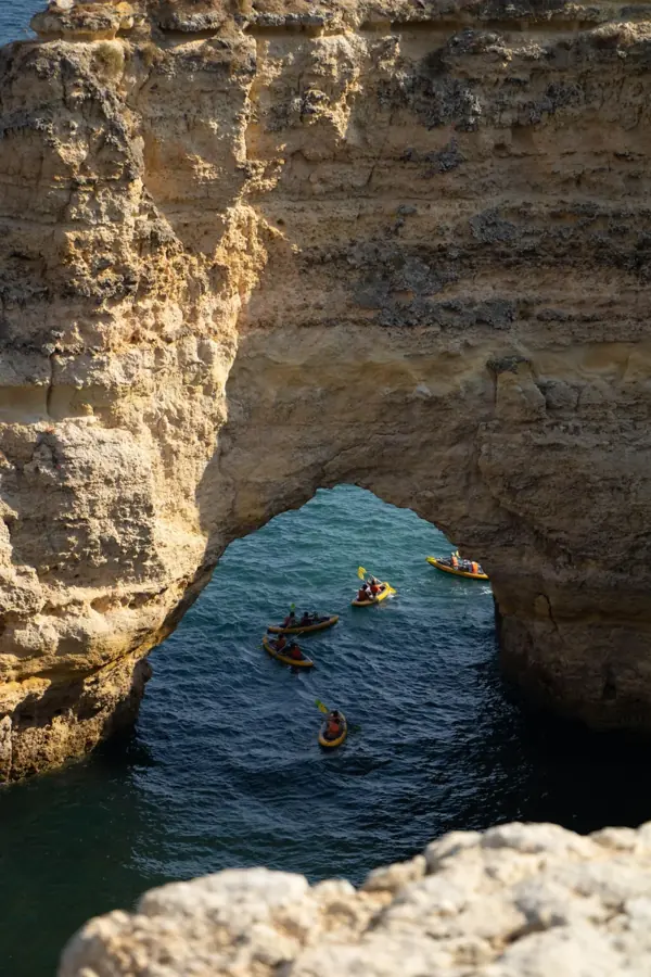 Kayak in fila sotto un grande arco naturale di calcare