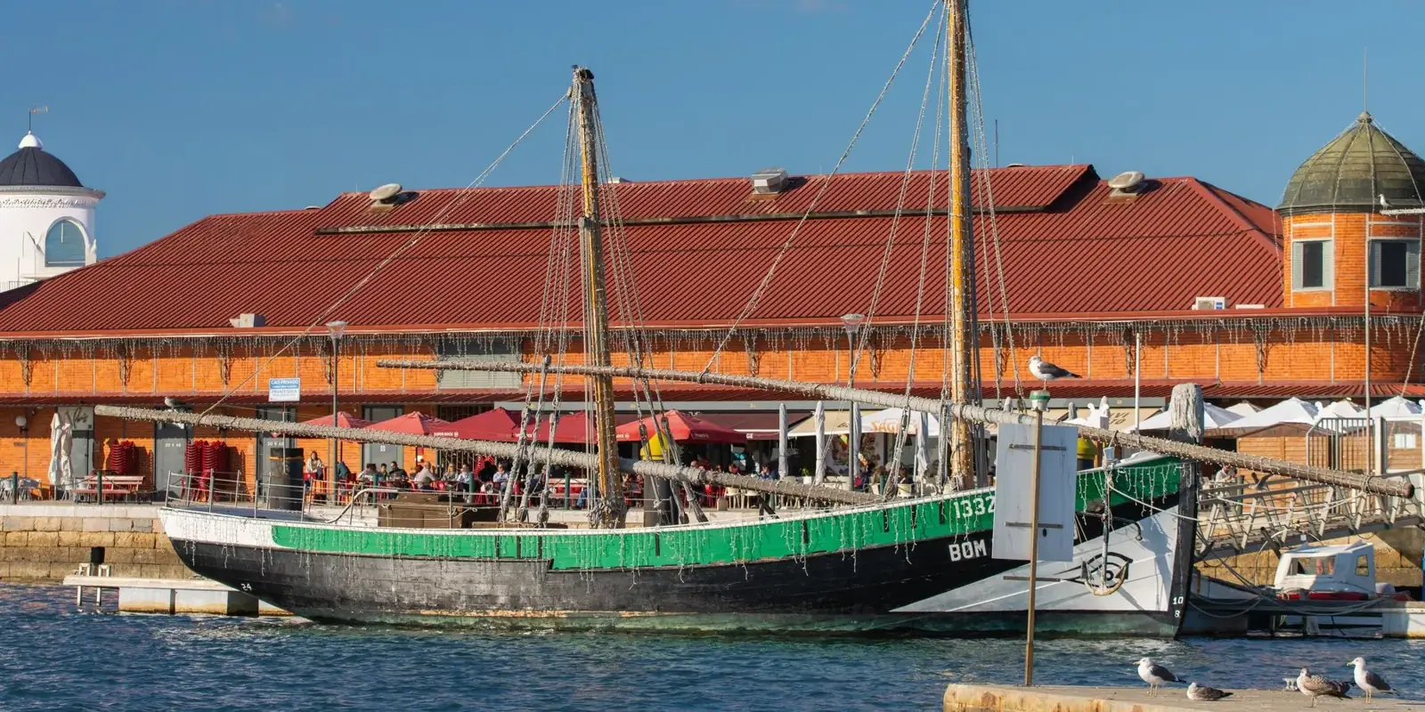 Una barca tradizionale davanti ai mercati in mattoni rossi sul lungomare di Olhão