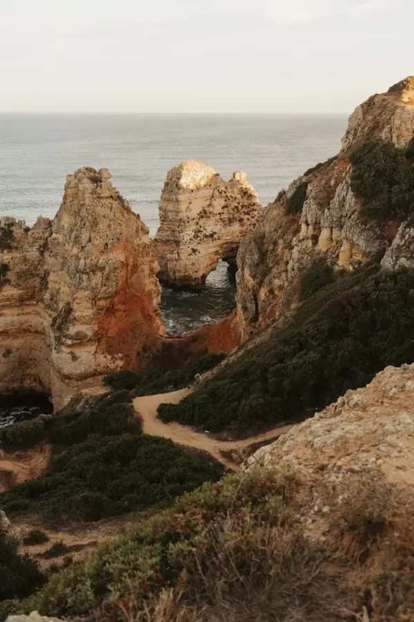 Un sentiero tra la macchia e le rocce dorate sopra l'oceano