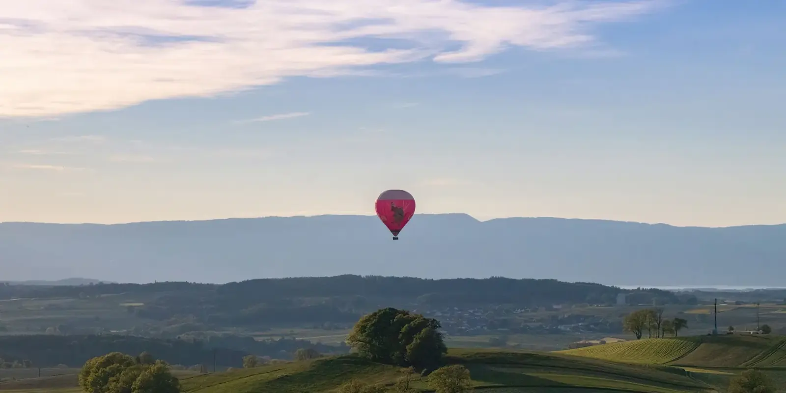 Una mongolfiera sopra colline verdi e campagna all'alba