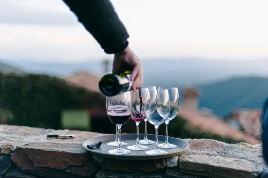 Vino rosso versato nei calici su un muretto di pietra, colline sullo sfondo