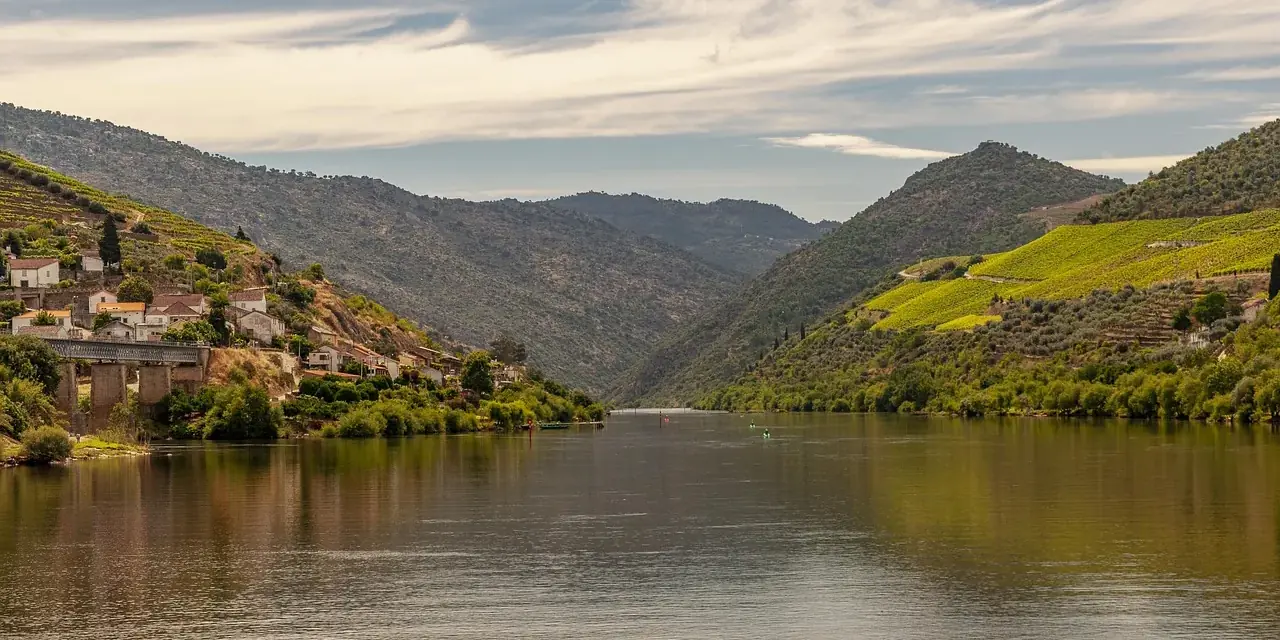 Il Douro calmo tra colline terrazzate, con le case di una quinta che si specchiano nell'acqua