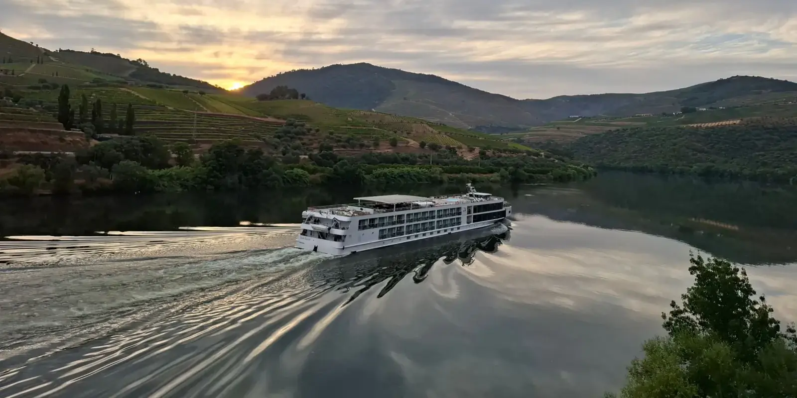 Una nave da crociera fluviale risale il Douro al tramonto tra le colline vitate