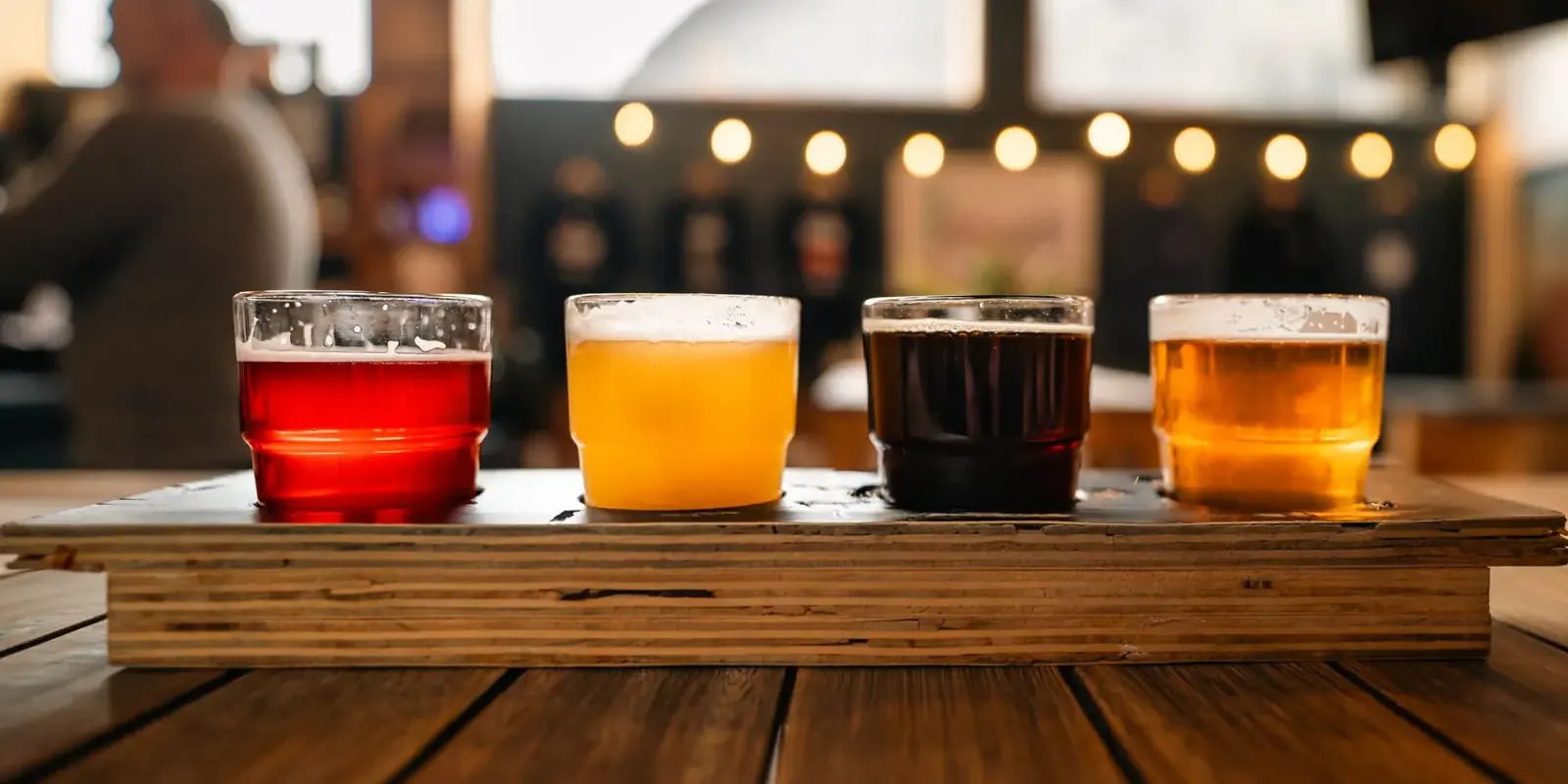 Quattro birre artigianali di colori diversi su un vassoio di legno al bancone