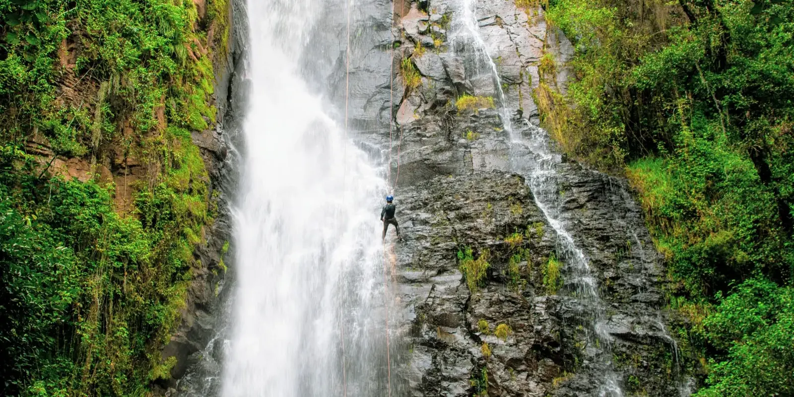 Una calata in corda accanto a una cascata tra pareti di roccia e vegetazione